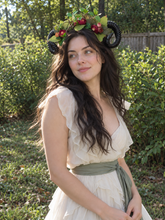 Load image into Gallery viewer, Three-quarter view of the black ram horns with green leaves and red flowers worn by a model with long dark hair in a cream dress outdoors (AI-generated model image)