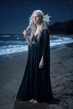 Load image into Gallery viewer, Full-body view of light blue mermaid fin ear cuffs worn by a model in a long dark dress standing on a beach at night (AI-generated model image)